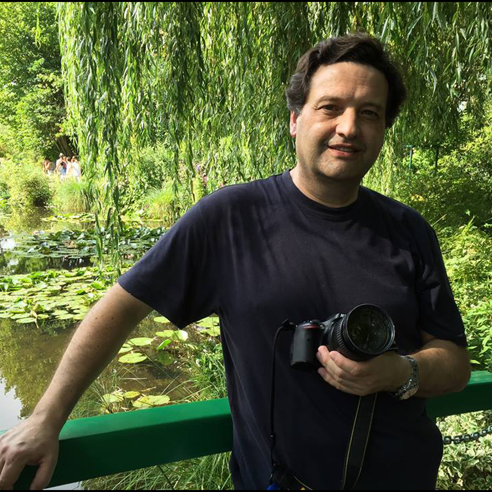 Miguel De Lanú artista visual chileno sosteniendo una cámara fotográfica en un jardín, retrato.