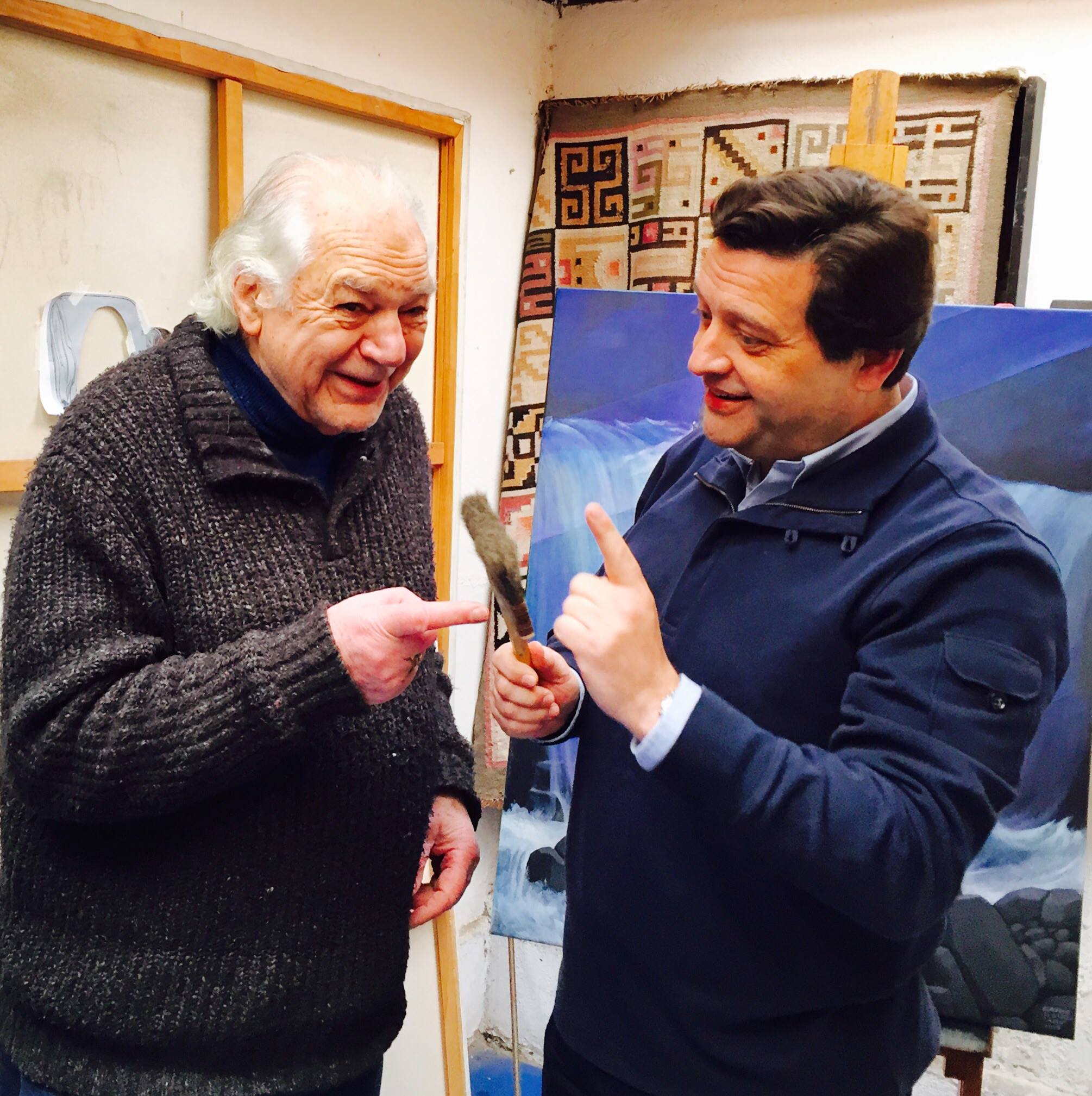 Miguel de Lanu, reconocido artista, conversa animadamente con el destacado actor chileno Claudio Di Girolamo en su estudio de arte. Diálogo entre dos figuras prominentes de la cultura chilena.