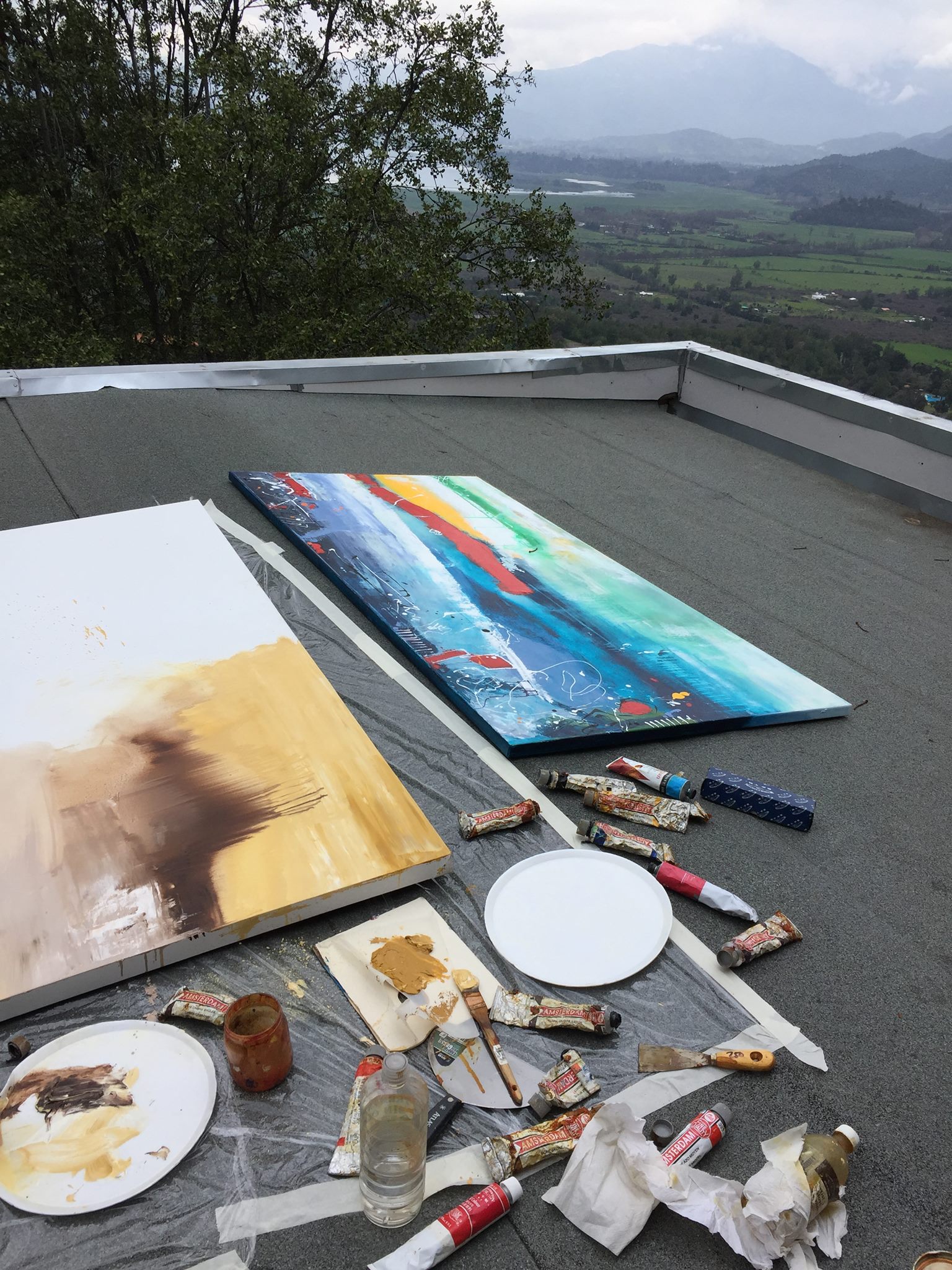 Miguel De Lanú, artista visual chileno: lienzos y materiales de pintura sobre un techo con vista al valle, proceso al aire libre