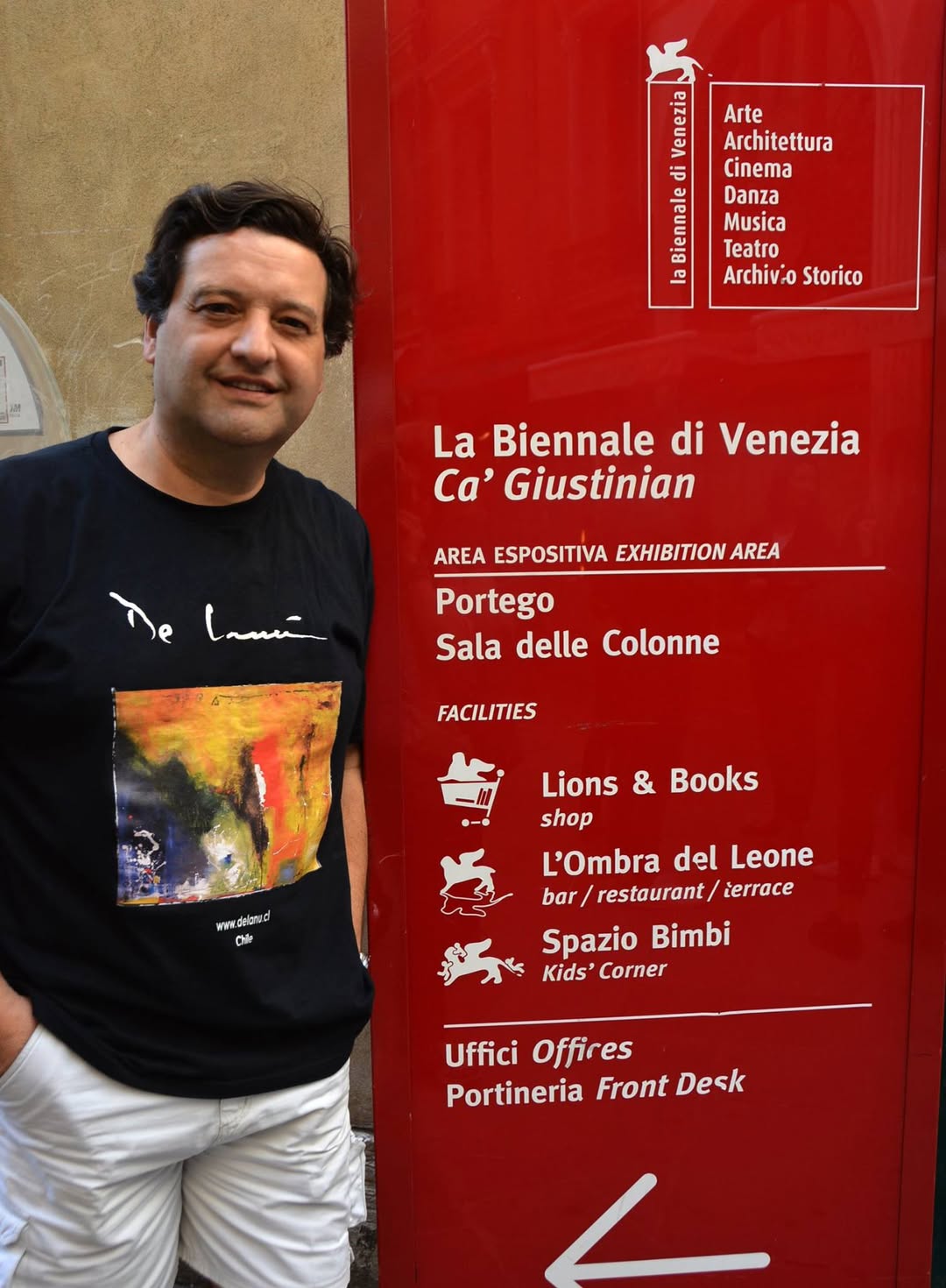 El pintor chileno artista Miguel De Lanú en la Bienal de Venecia, junto al cartel de la exhibición de arte internacional.